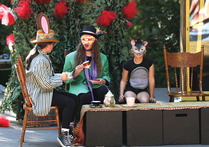 Three young actors sip tea on stage for a theatre production