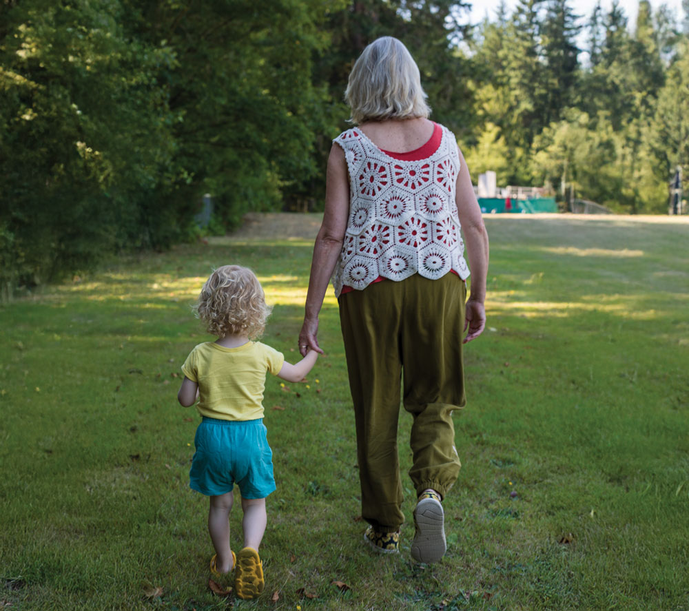 Young child holds hands with woman as they walk away from the camera