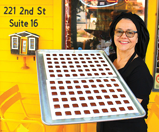 Woman holds tray of chocolate in front of yellow store