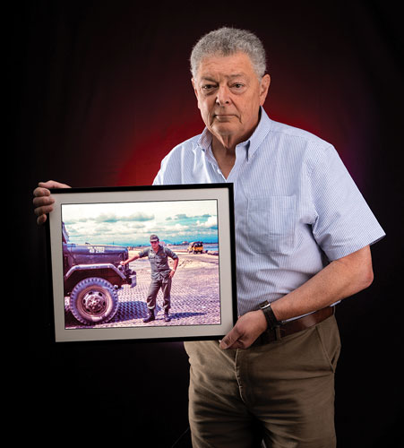 Man holding photo of himself at an earlier age standing with a truck