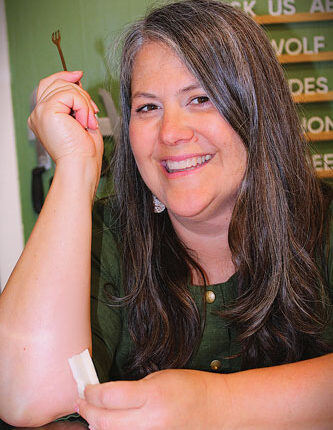Woman with her arms on a counter holds a tiny cheese fork