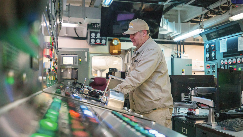 Man in tan work clothes works colorful controls of ferry boat