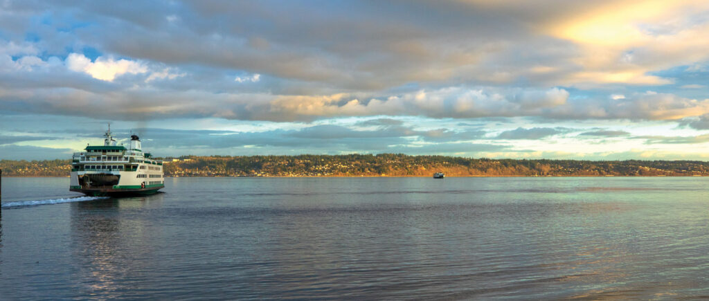 Green and white ferry boat sails toward land while oncoming ferry sails in the distance