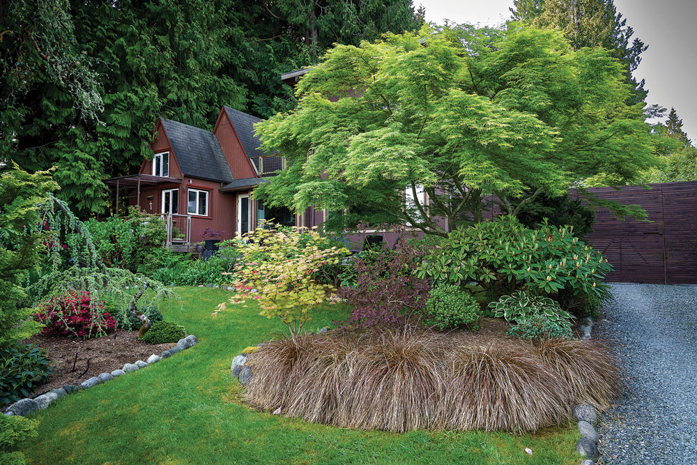 Lawn and small trees in front of red cottage in the background