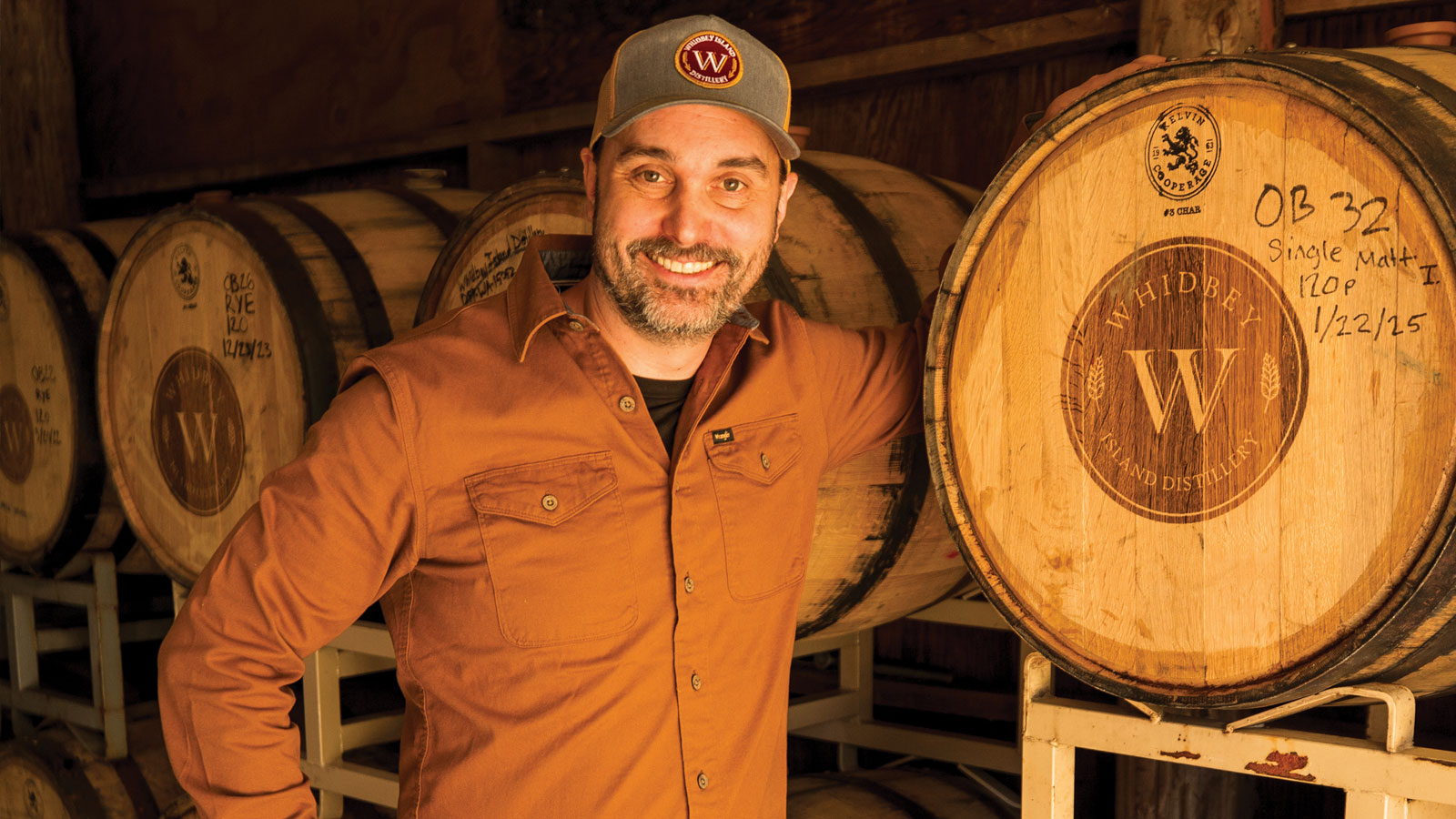 Man at a distillery standing in front of oak casks