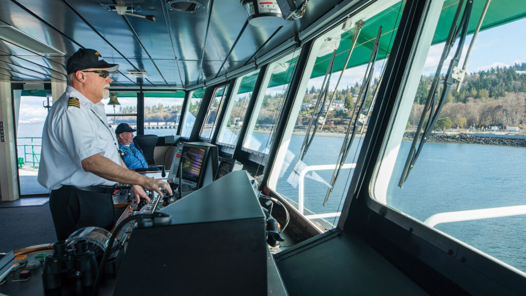 Man at the helm of a ferry docking at the ferry landing.