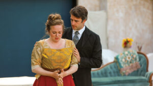 Dramatic theatre performance of woman embraced by man in suit and tie.