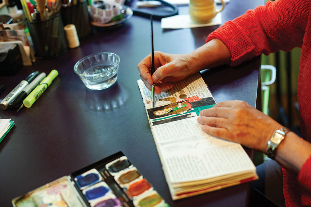 Closeup of a woman's hands as she paints watercolor illustrations in a handmade booklet