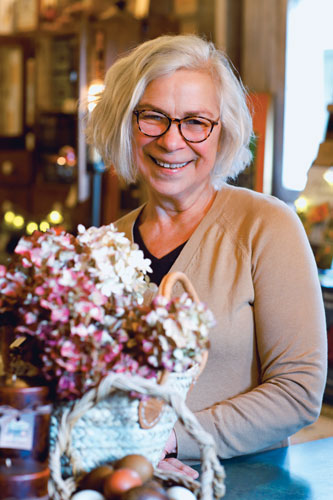 Older woman smiles while holding basket with white and pink flowers