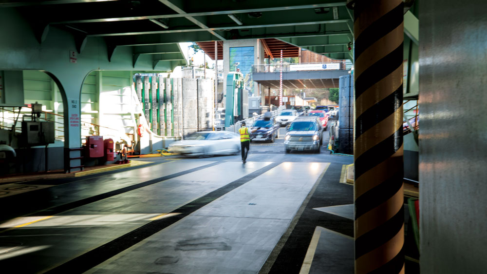 Motion blur of cars driving to load onto ferry with one crew member in front guiding cars