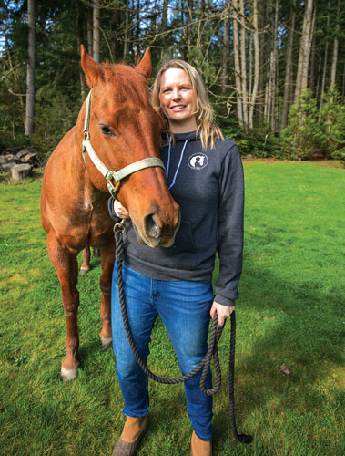 Brown horse nuzzles woman wearing a grey sweatshirt and blue jeans