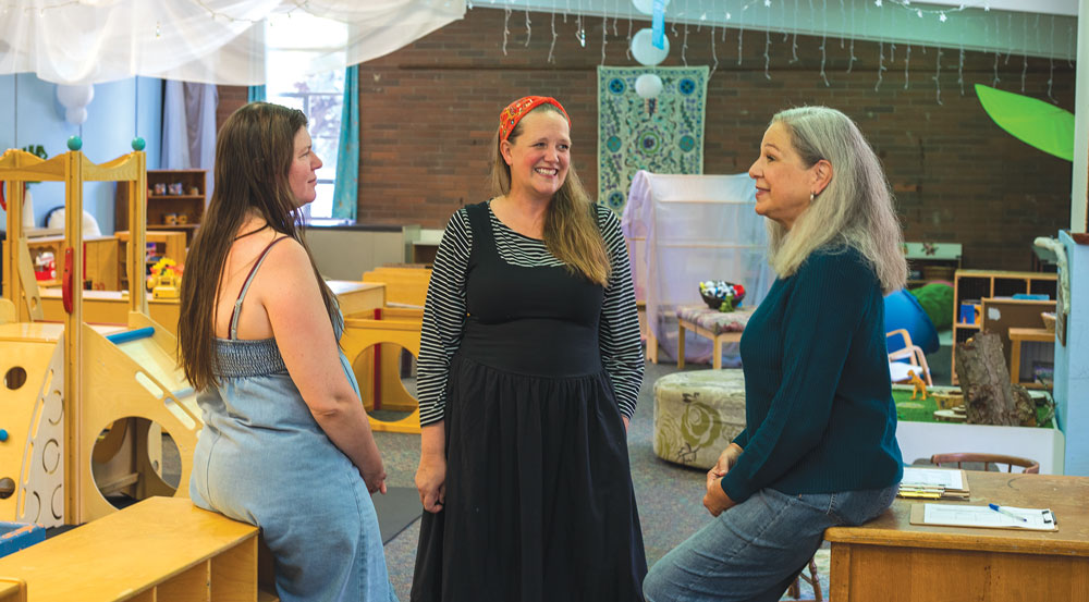 Three women sitting in a children's play room talk with each other