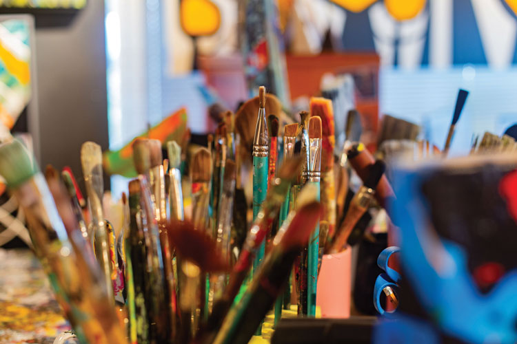 Array of paint brushes with colorful paintings blurred in the background