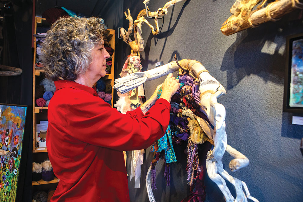 Older woman in bright red shirt hangs driftwood and woven artwork